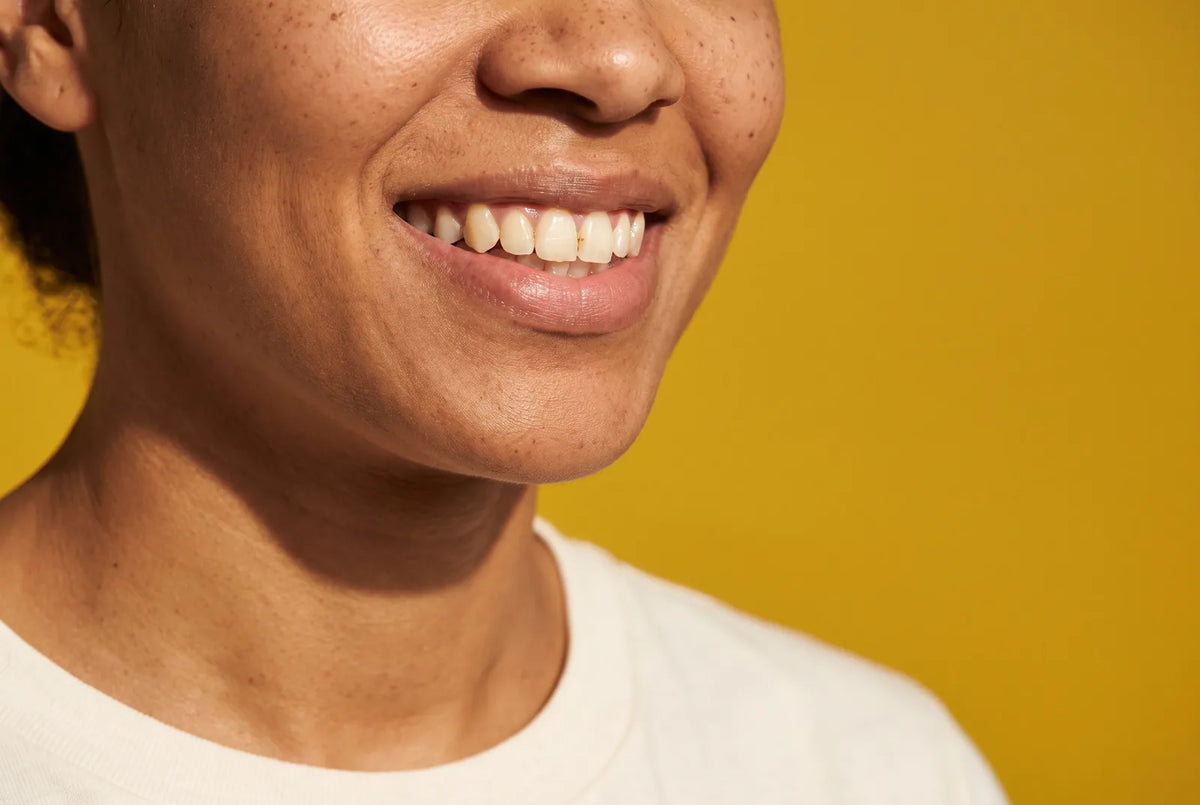 An illustrative close-up of a relaxed, natural smile in warm sunlight against a yellow background.