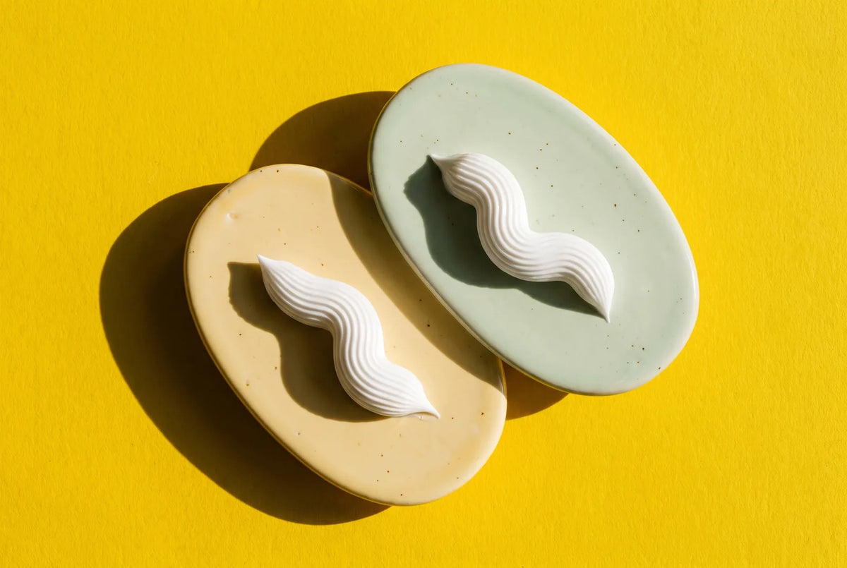 Two sculptural white toothpaste ribbons on cream and mint ceramic tiles against a yellow background.