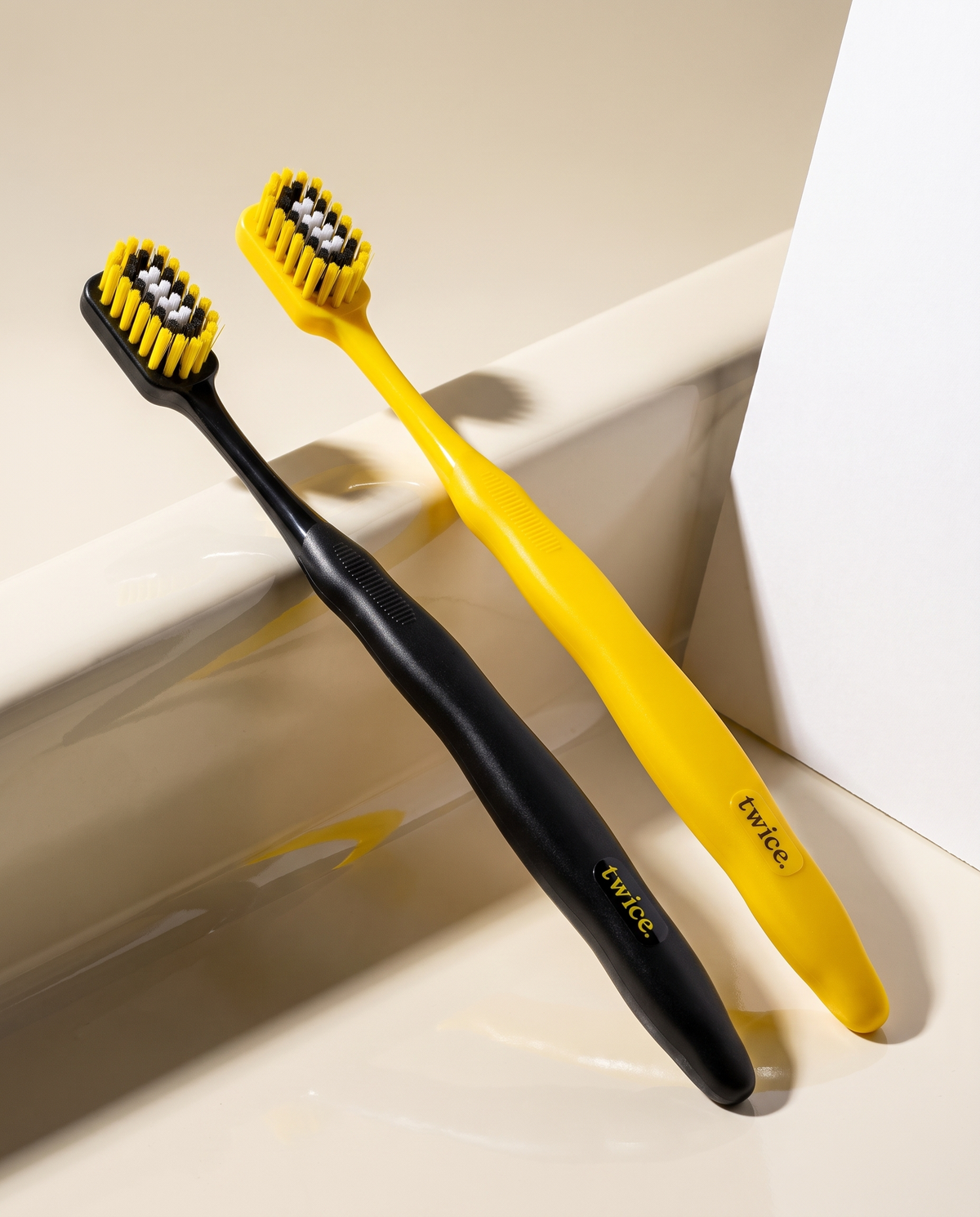 Black and yellow Stadium toothbrushes resting on a ceramic ledge.