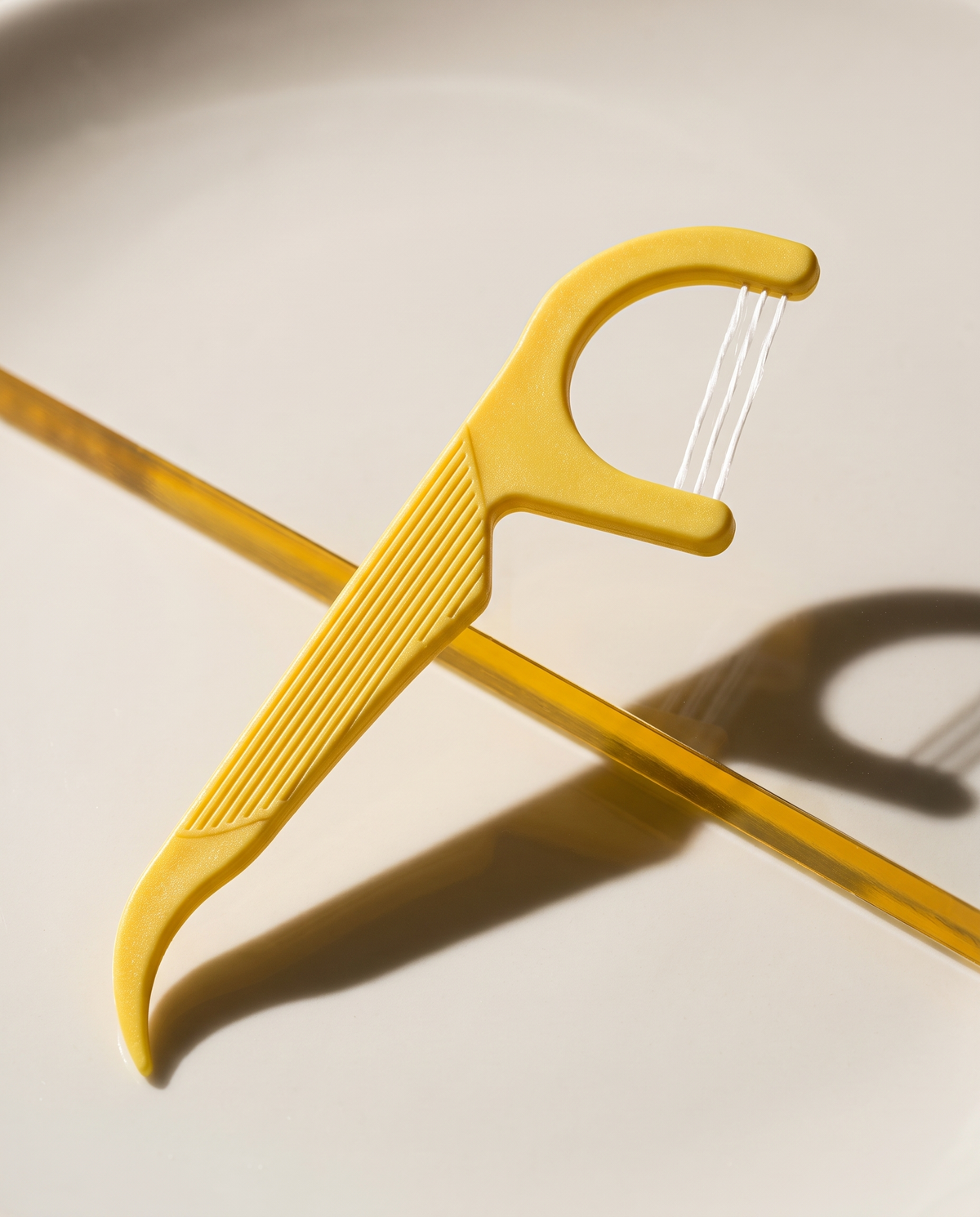 Yellow three-strand floss pick on a ceramic surface.