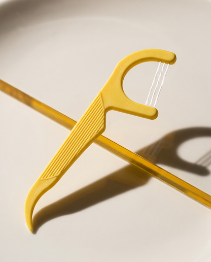 Yellow three-strand floss pick on a ceramic surface.